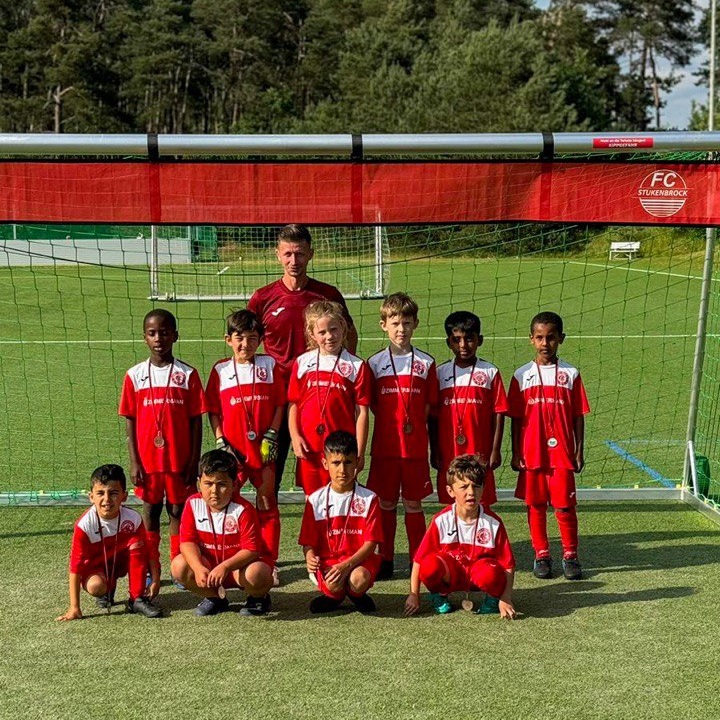 Team von Jugendspielern mit Trainer posieren vor einem Fußballtor